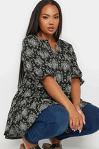 Desenli siyah oversize bluz ve kot pantolon giyen büyük beden kadın model oturuyor