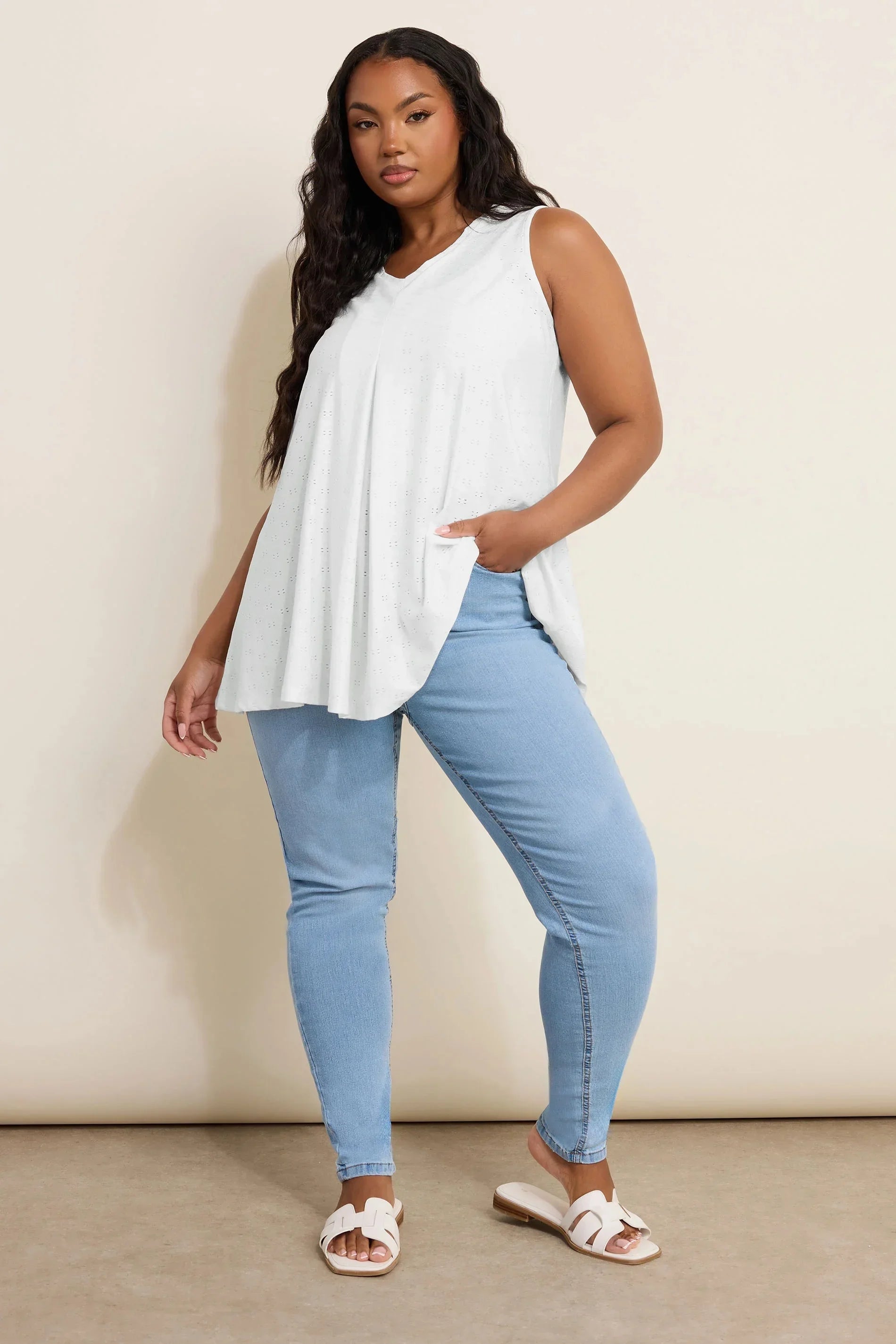 Büyük beden kadın modası, beyaz kolsuz bluz ve açık mavi skinny kot pantolon kombinli model.
